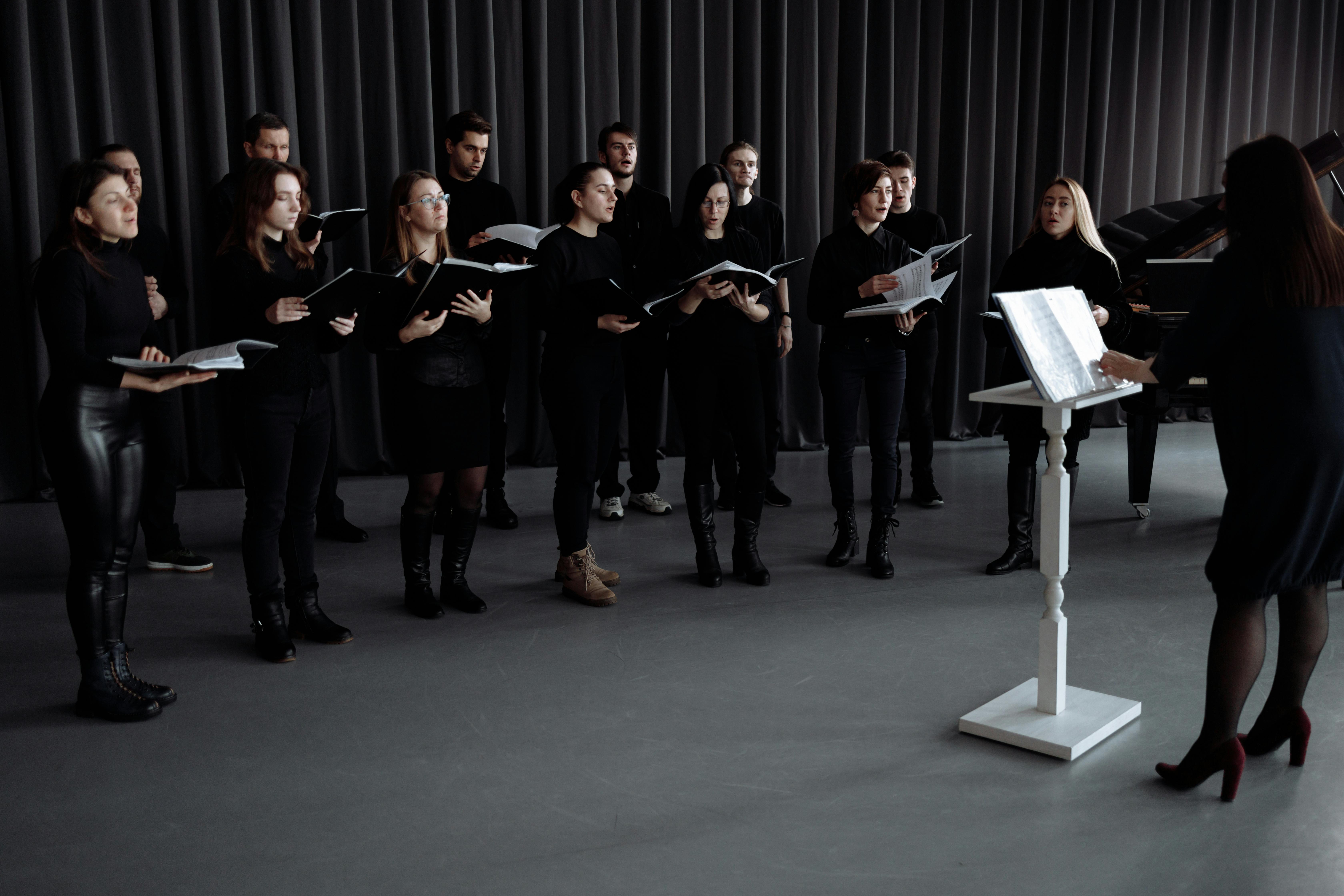 Choir ensemble rehearsing in all black with a conductor at a music stand